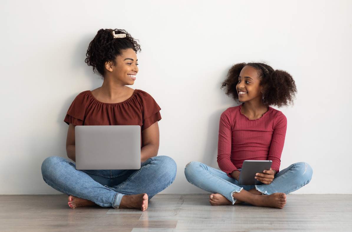 mère assise avec un ordinateur portable et souriant à sa fille qui est sur sa tablette