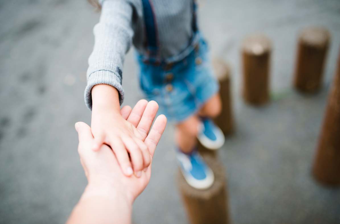 child hoping across logs holding parents hand