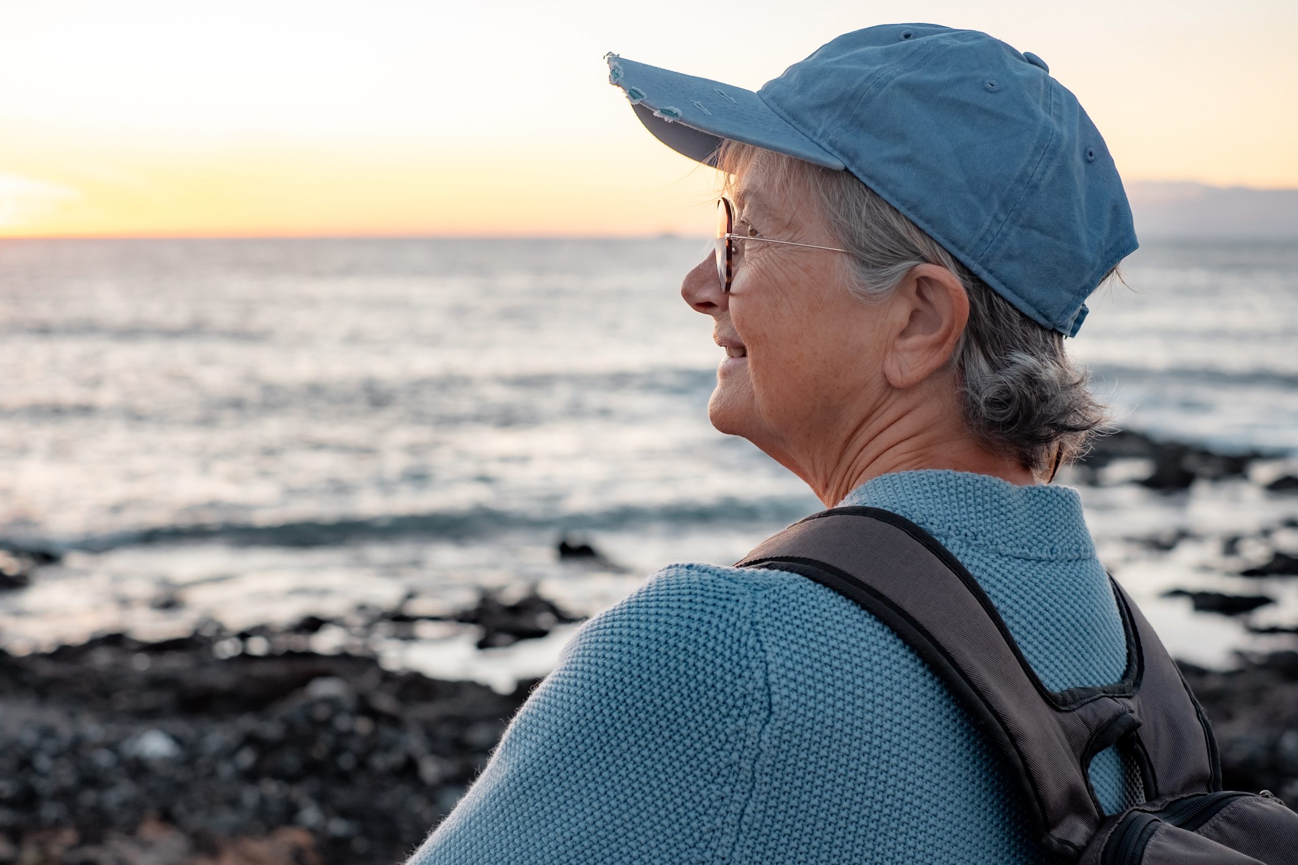 Older woman staring out at water wearing a blue hat and blue shirt